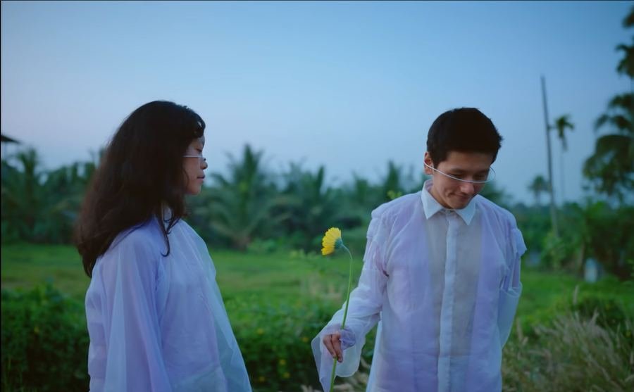 Still from Yellow Paper Daisy: a couple in white with a yellow daisy in a Kerala field